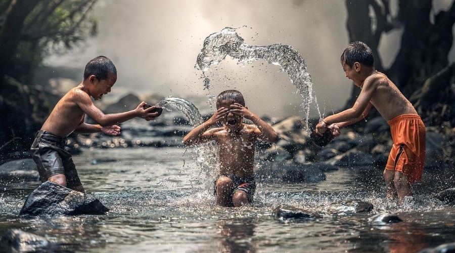 decorative boys splash around in a river in south east asia
